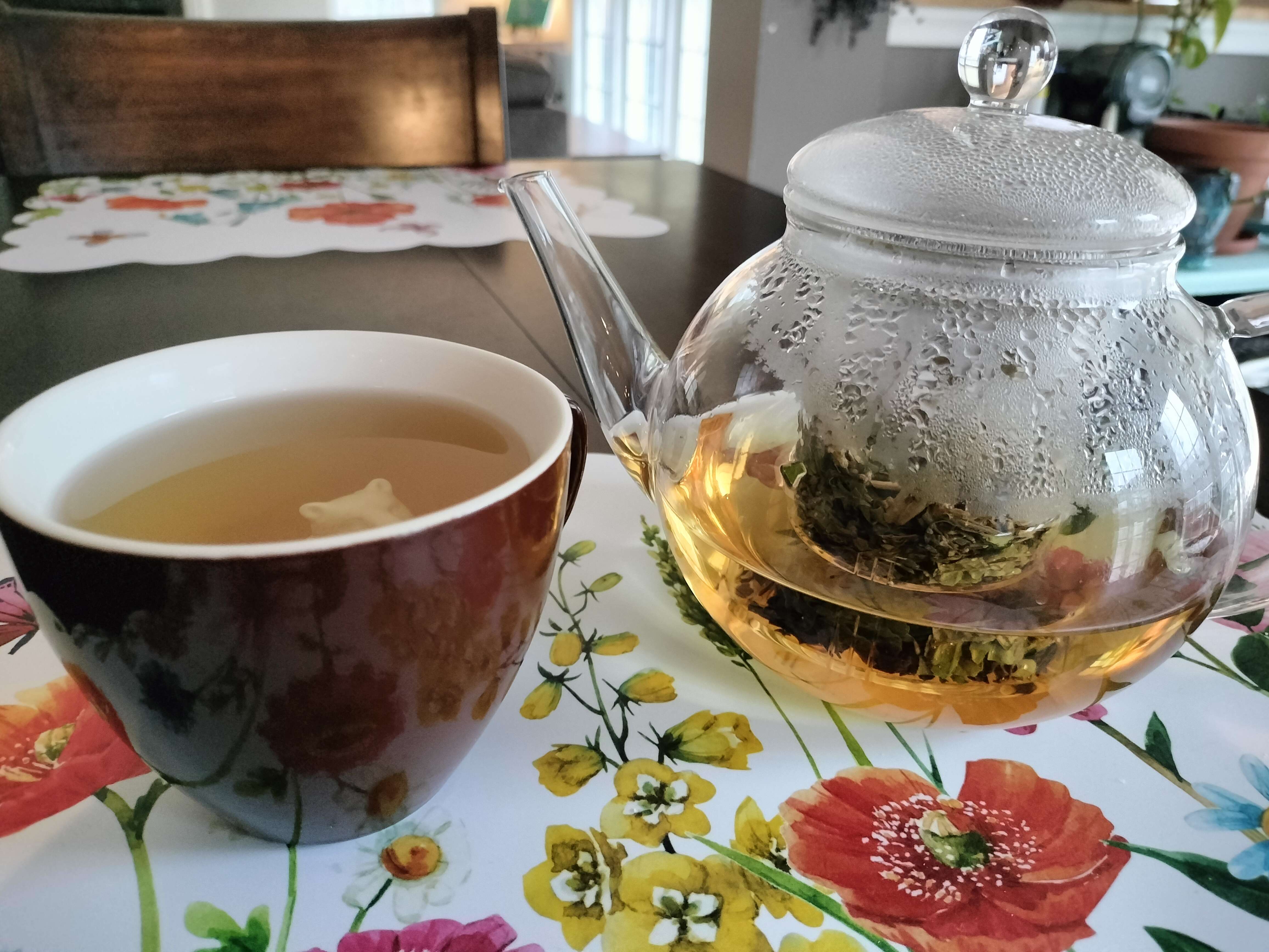 A full cup of tea, next to a mostly-empty glass teapot. Steam obscures the inside of the teapot, but you can see tea leaves held in an infuser inside it. In the cup, you can just barely see the head of a bear figure peeking out.